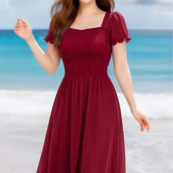Woman wearing a burgundy dress on a beach with ocean and sky in the background