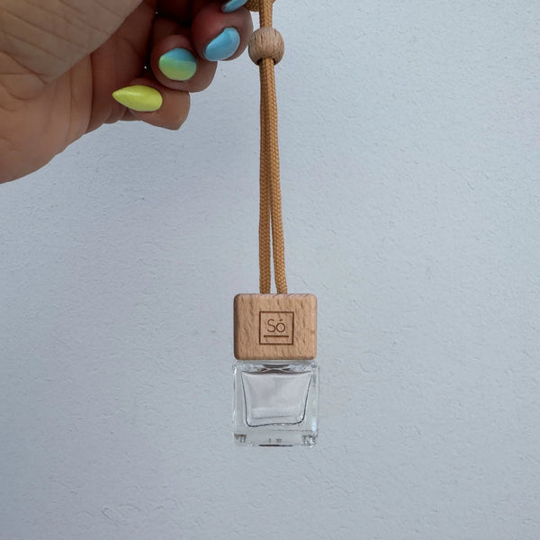 Clear glass pendant with wooden tag held by a hand against a light gray background