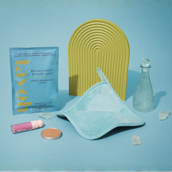 Makeup removal products including a reusable makeup remover cloth, bottle, and other items on a blue background.