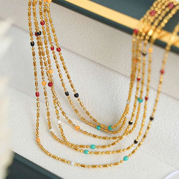 A close-up of a multi-strand gold beaded necklace with small colorful accent beads, displayed on a white jewelry box.