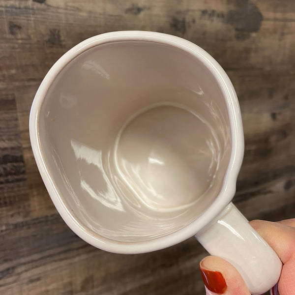 White mug held by a hand on a wooden surface