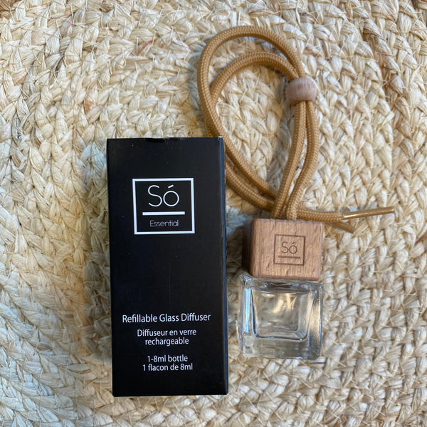 Scent bottle with wooden cap and clear glass, black box labeled 'só', on a textured beige surface.