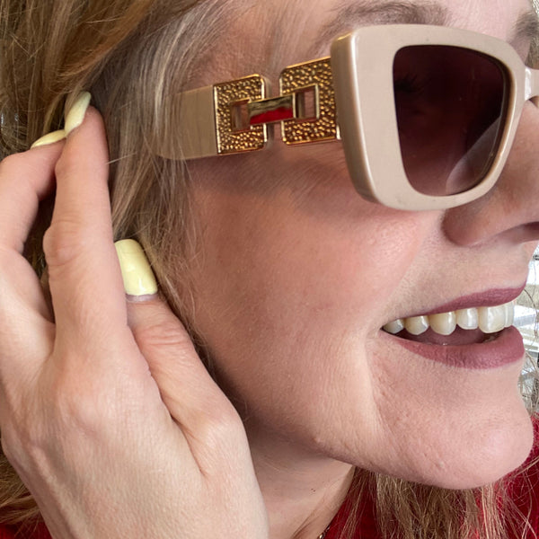 Close-up of a person wearing a gold bracelet with a red logo on a red background