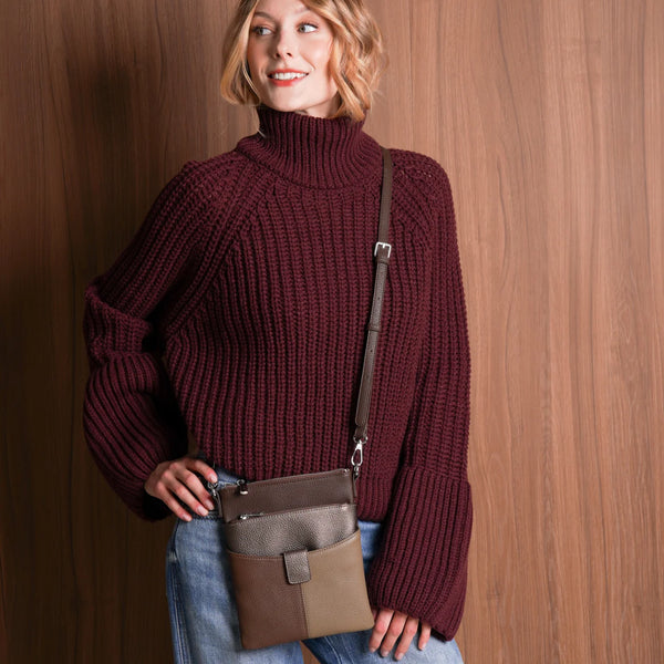 Woman wearing a maroon sweater and blue jeans, holding a brown bag against a wooden wall.