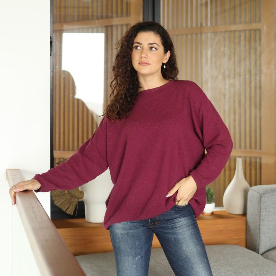 Woman wearing a maroon sweater and blue jeans standing in a living room.