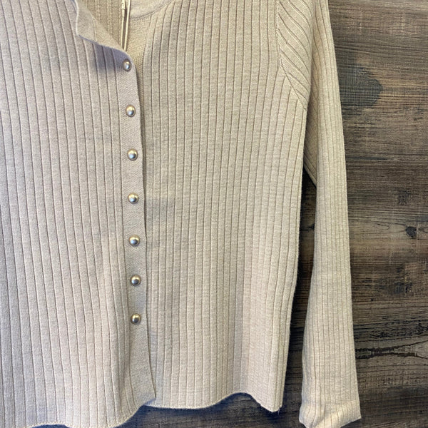 A ribbed knit long-sleeve top in a light beige or cream color, featuring a button-down front with metallic buttons, laid flat on a dark wood background.