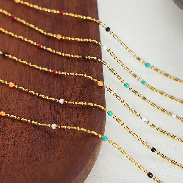 Gold beaded necklaces with small multicolor accent beads, draped over a dark wooden surface on a white background.