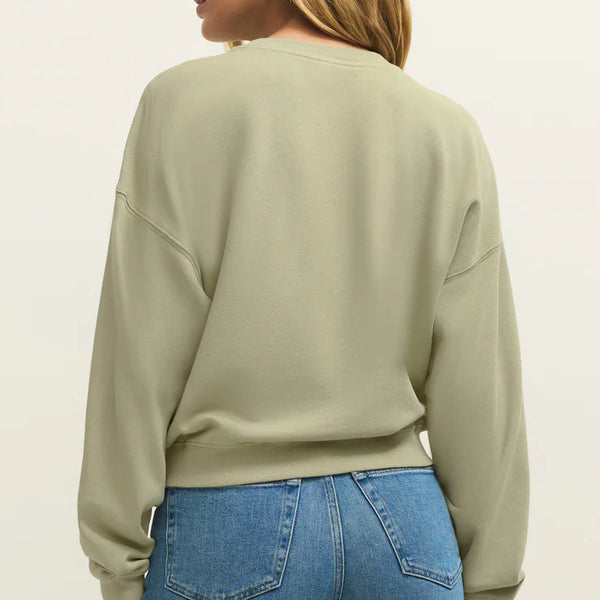 Woman wearing a light green sweatshirt and blue jeans on a plain background