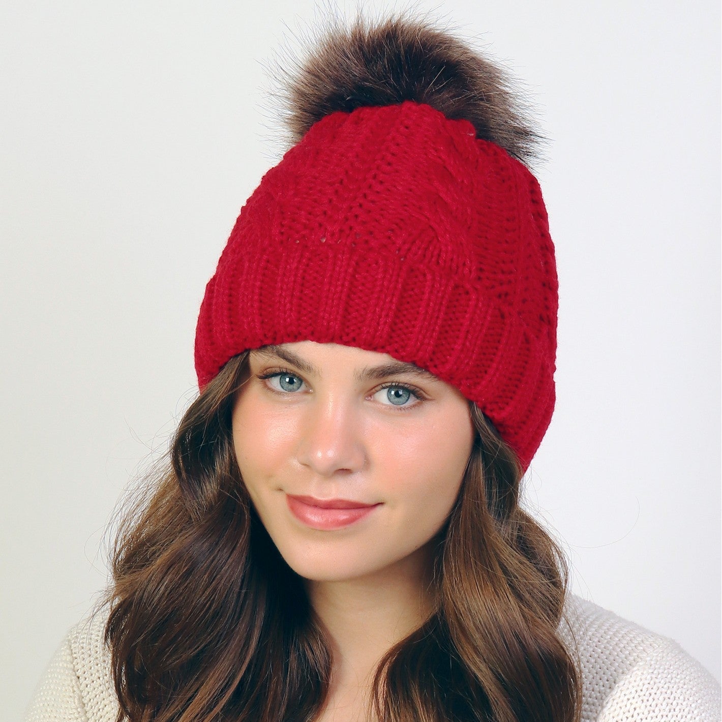 Woman wearing a red knitted beanie with a fur pom-pom on a white background