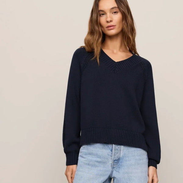 A woman modeling a dark navy blue long-sleeve knit sweater and light-wash wide-leg denim jeans against a plain beige studio background.