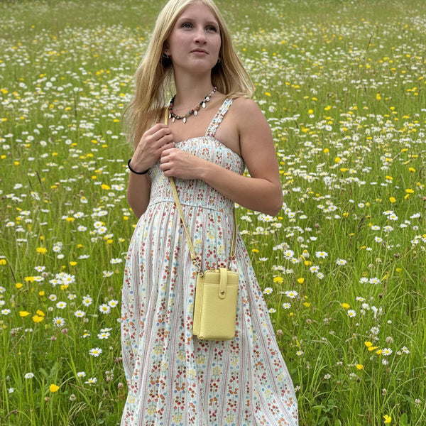 Woman in a floral dress holding a yellow purse in a field of wildflowers