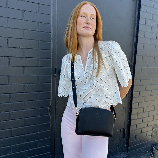 Woman wearing a white blouse and black handbag against a brick wall.