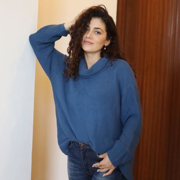 Woman wearing a blue sweater standing against a wooden door.