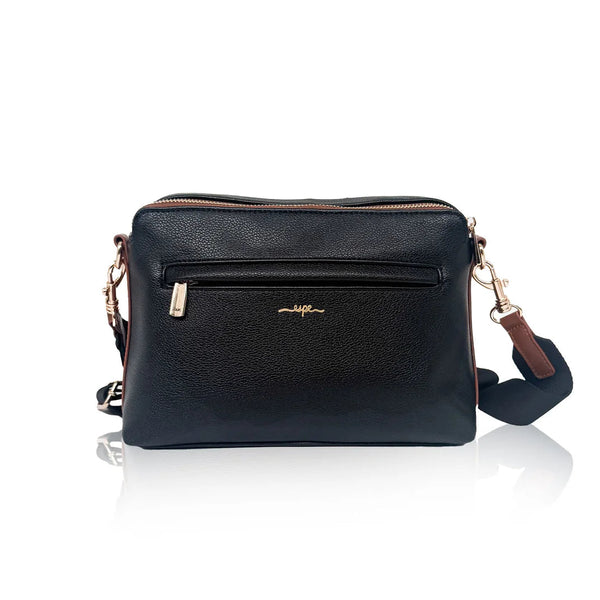 A black pebbled leather crossbody bag with a front zippered pocket, gold-tone hardware, and a brown leather accent tab, shown on a reflective white background.