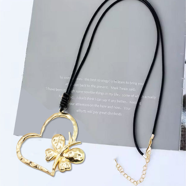 Gold butterfly pendant on a heart-shaped frame with a black cord, placed on a textured surface.