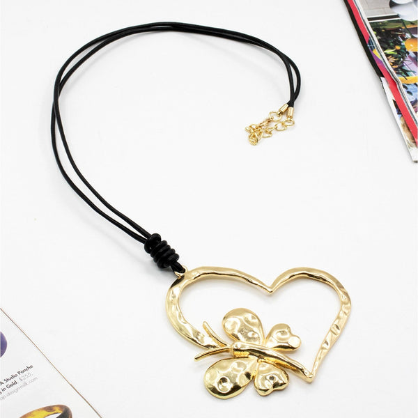 Gold heart-shaped pendant with butterfly design on a black cord against a white background.