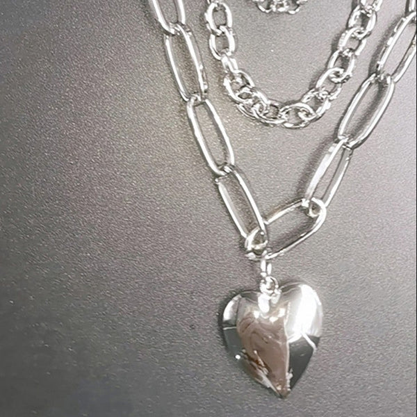 Stack of silver chain necklaces with a heart pendant on a gray background