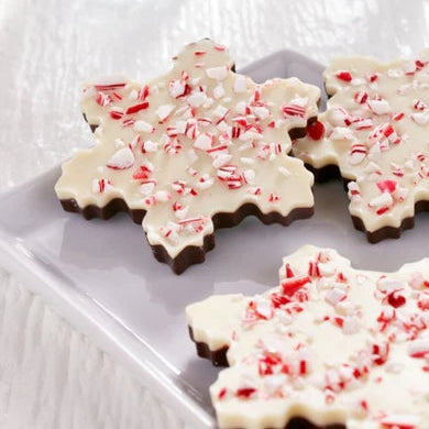 Snowflake-shaped cookies with white chocolate and peppermint candy on a white surface.
