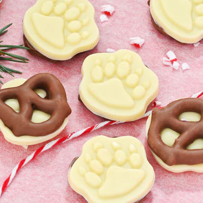 Decorative cookies shaped like pretzels and paw prints on a pink surface with Christmas decorations.