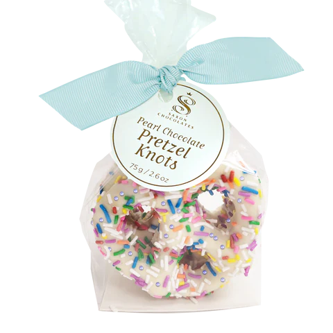 Packaged pearl chocolate pretzel knots with colorful sprinkles and a light blue ribbon on a white background.