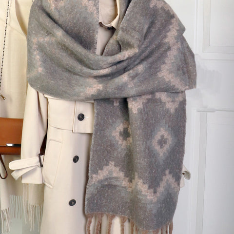 Gray patterned scarf with fringes draped over a white coat on a hanger.