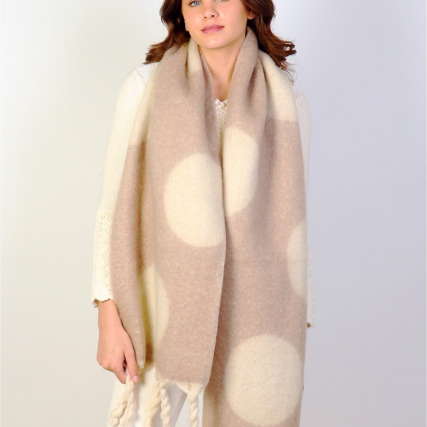 Woman wearing a beige and white polka dot scarf on a plain background