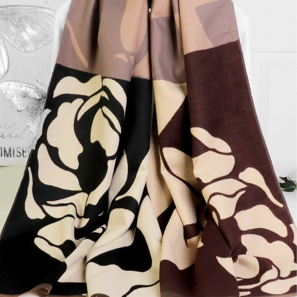 A long scarf draped over a hanger, featuring a color-blocked design with abstract floral patterns in beige, brown, black, and cream.
