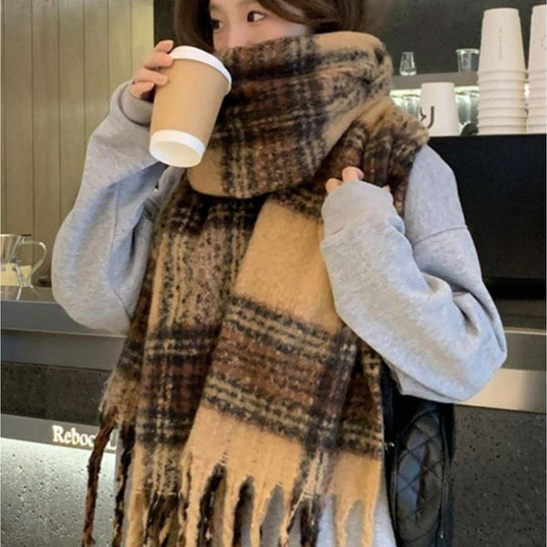 Person wearing a large plaid scarf and holding a coffee cup in an indoor setting.