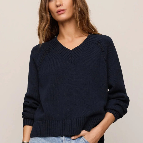 Woman wearing a navy sweater and light blue jeans against a beige background