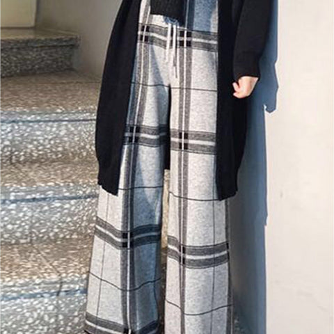 Person wearing a black coat and plaid pants standing on a staircase.