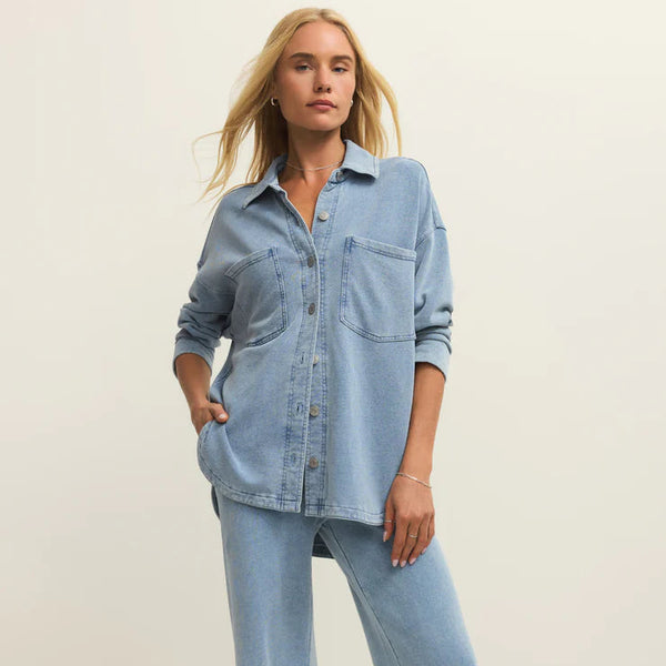 Woman wearing a light blue denim shirt and jeans on a plain background