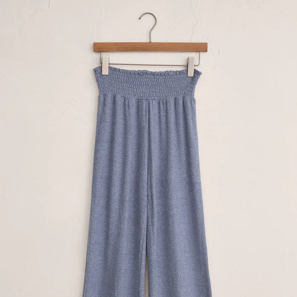 Blue pants hanging on a wooden hanger against a white background