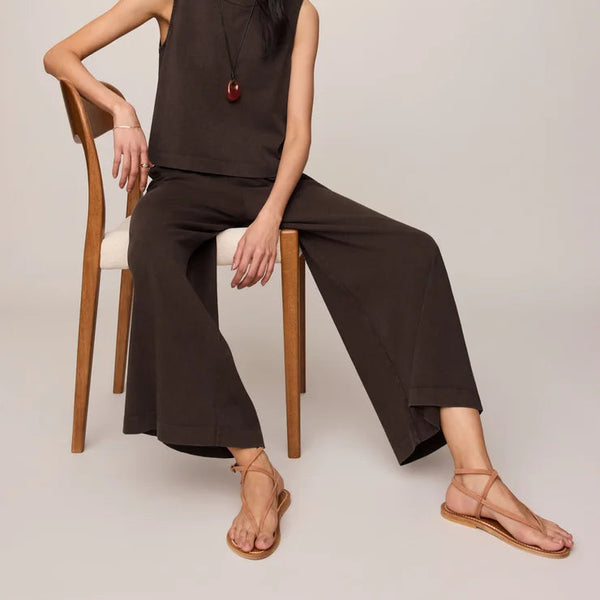 Woman sitting on a chair wearing a brown outfit against a plain background