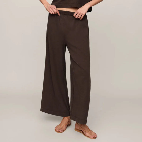 A woman modeling a dark brown sleeveless crop top and matching wide-leg pants against a plain light beige studio background.