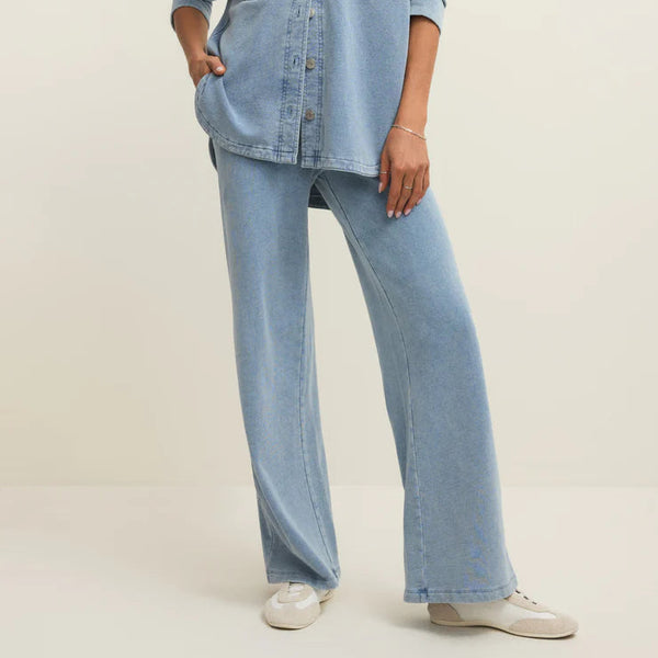 Woman wearing a light blue denim shirt and jeans on a plain background
