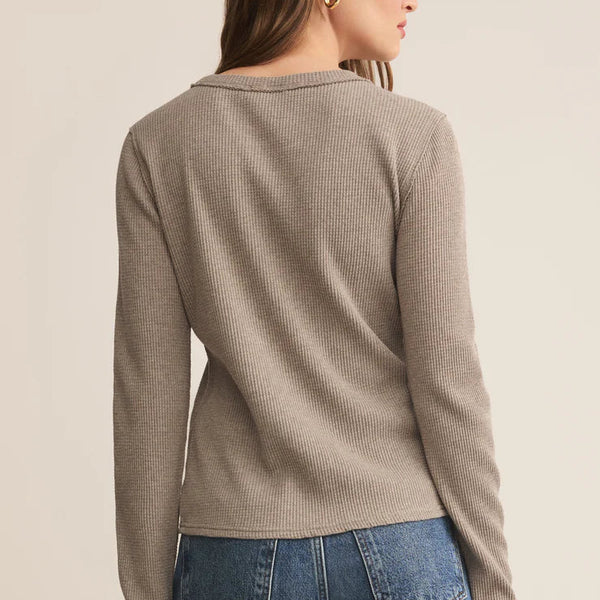 Woman wearing a beige sweater and blue jeans on a beige background