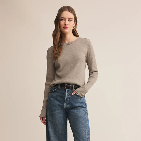 Woman wearing a beige sweater and blue jeans on a beige background