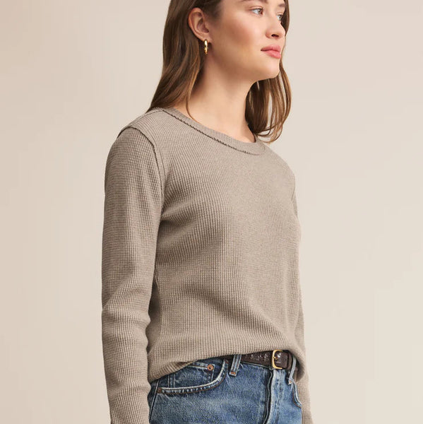 Woman wearing a beige sweater and blue jeans against a plain background