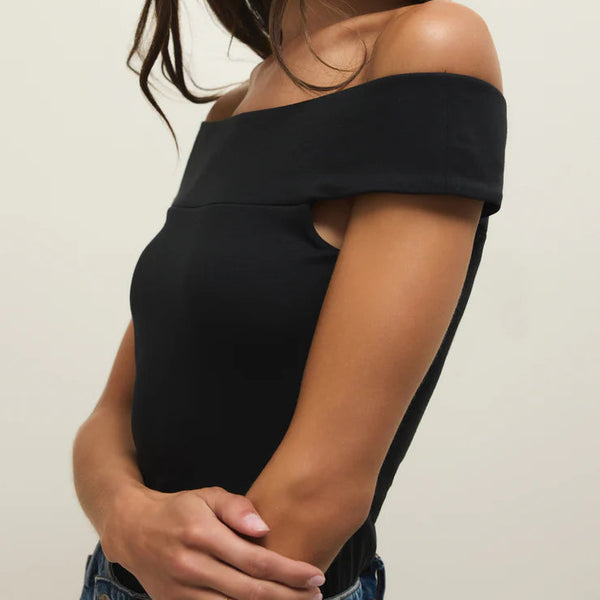 Woman wearing a black off-shoulder top against a plain background