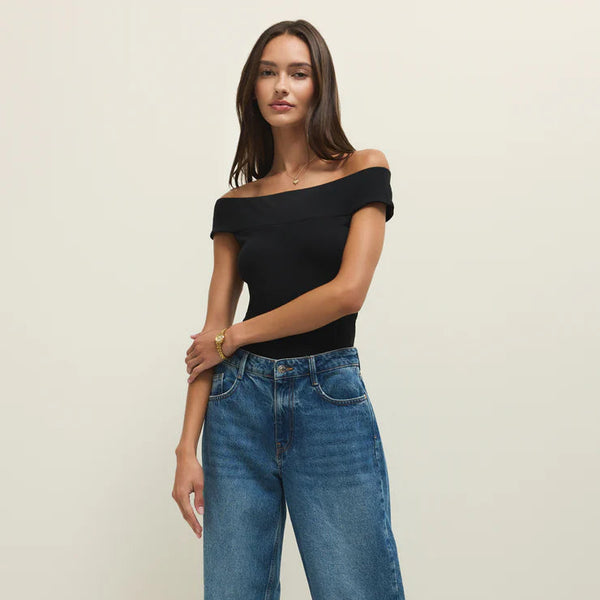 Woman wearing a black off-shoulder top and blue jeans on a plain background