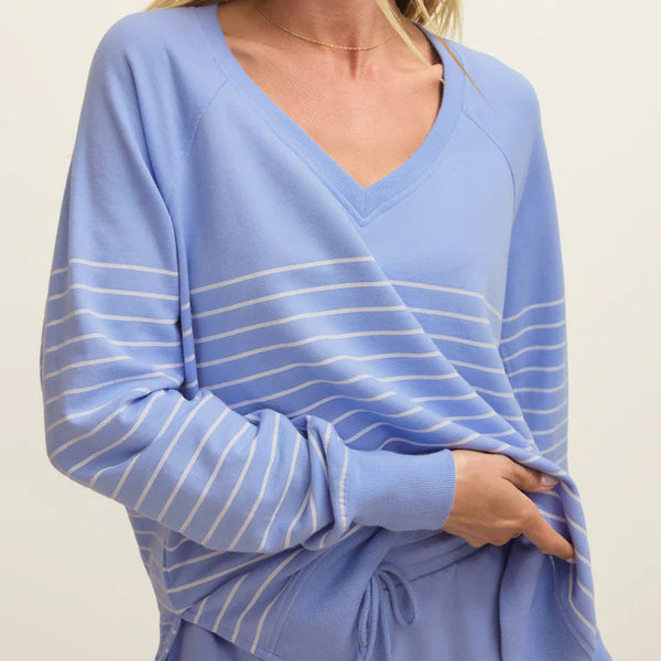 Woman wearing a light blue long-sleeve top with white stripes on a plain background