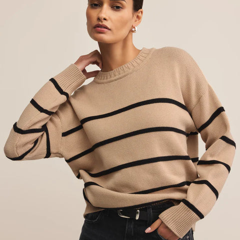 Woman wearing a beige sweater with black stripes against a plain background