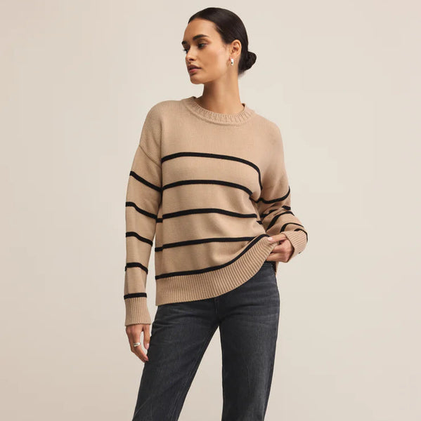 Woman wearing a beige sweater with black stripes and dark jeans on a beige background
