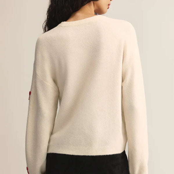 Woman wearing a cream sweater and black skirt on a plain background