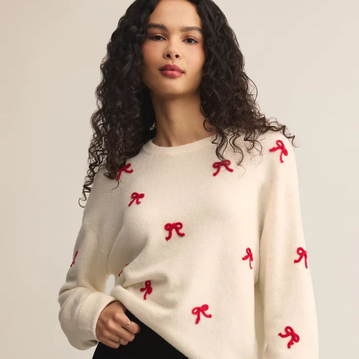Woman wearing a cream sweater with red bow patterns on a plain background