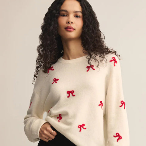 Woman wearing a cream sweater with red bow patterns on a plain background