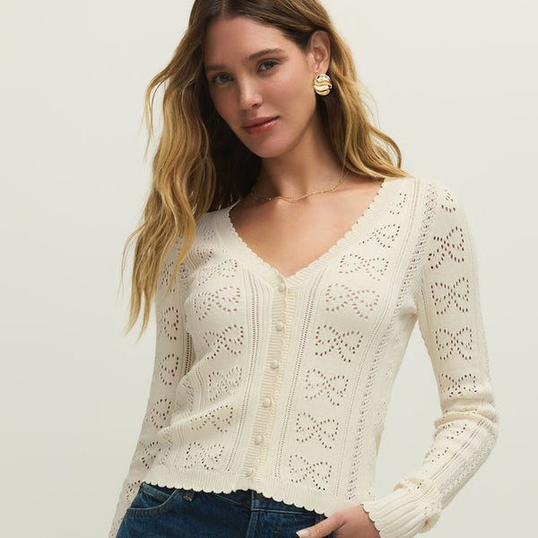 Woman wearing a white lace cardigan and blue jeans on a plain background