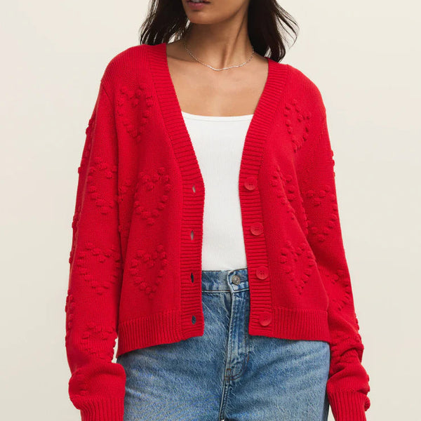 Woman wearing a red cardigan over a white top and blue jeans on a beige background