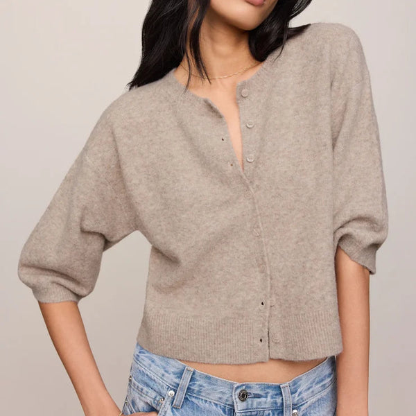 Woman wearing a beige button-up shirt and blue jeans against a plain background