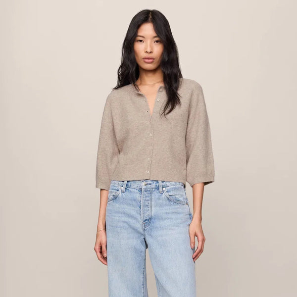 Woman wearing a beige shirt and light blue jeans against a plain background